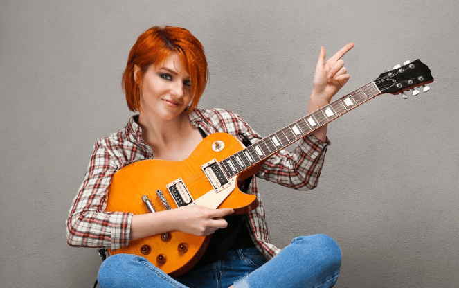 Guitarrista concentrado tocando una guitarra eléctrica negra junto a una ventana