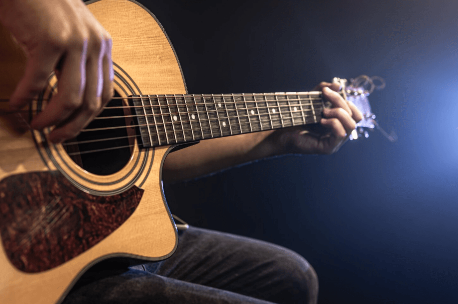 Primer plano de una guitarra acústica tocada en un entorno oscuro con luz azul de escenario