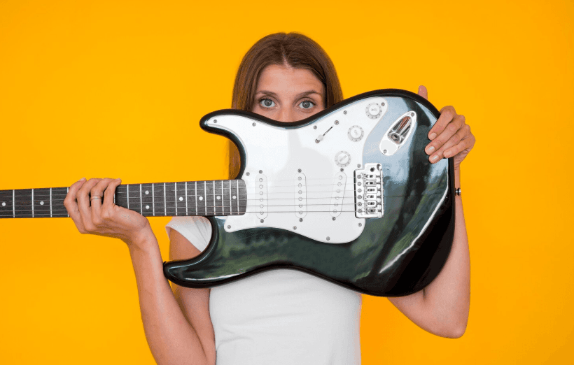 Persona sosteniendo una guitarra eléctrica negra frente a un fondo amarillo